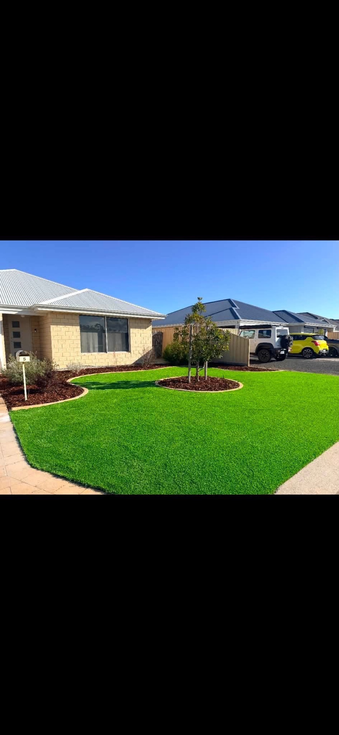 The same front yard reborn as a lush green lawn with a feature tree, after installation.